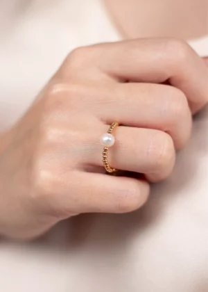 Gros plan de la bague ajustable Ondée en plaqué or 3 microns avec une perle de culture blanche, portée sur une main.