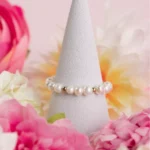 Bague ajustable Sirena en perles de culture blanches et détails dorés, présentée sur un support parmi des fleurs roses.
