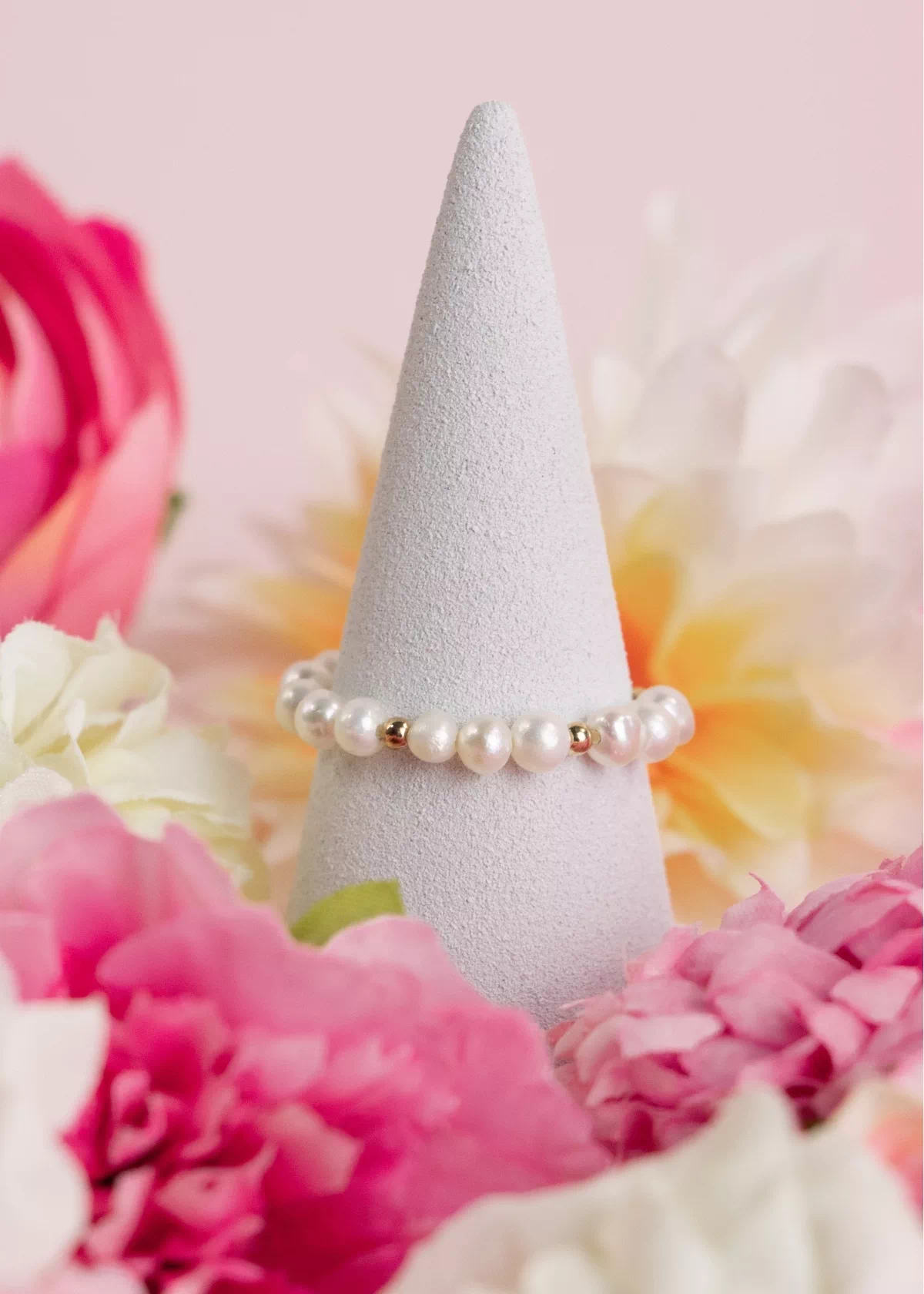 Bague ajustable Sirena en perles de culture blanches et détails dorés, présentée sur un support parmi des fleurs roses.