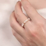 Gros plan de la bague ajustable Sirena en perles de culture blanches et détails dorés, portée sur un doigt.