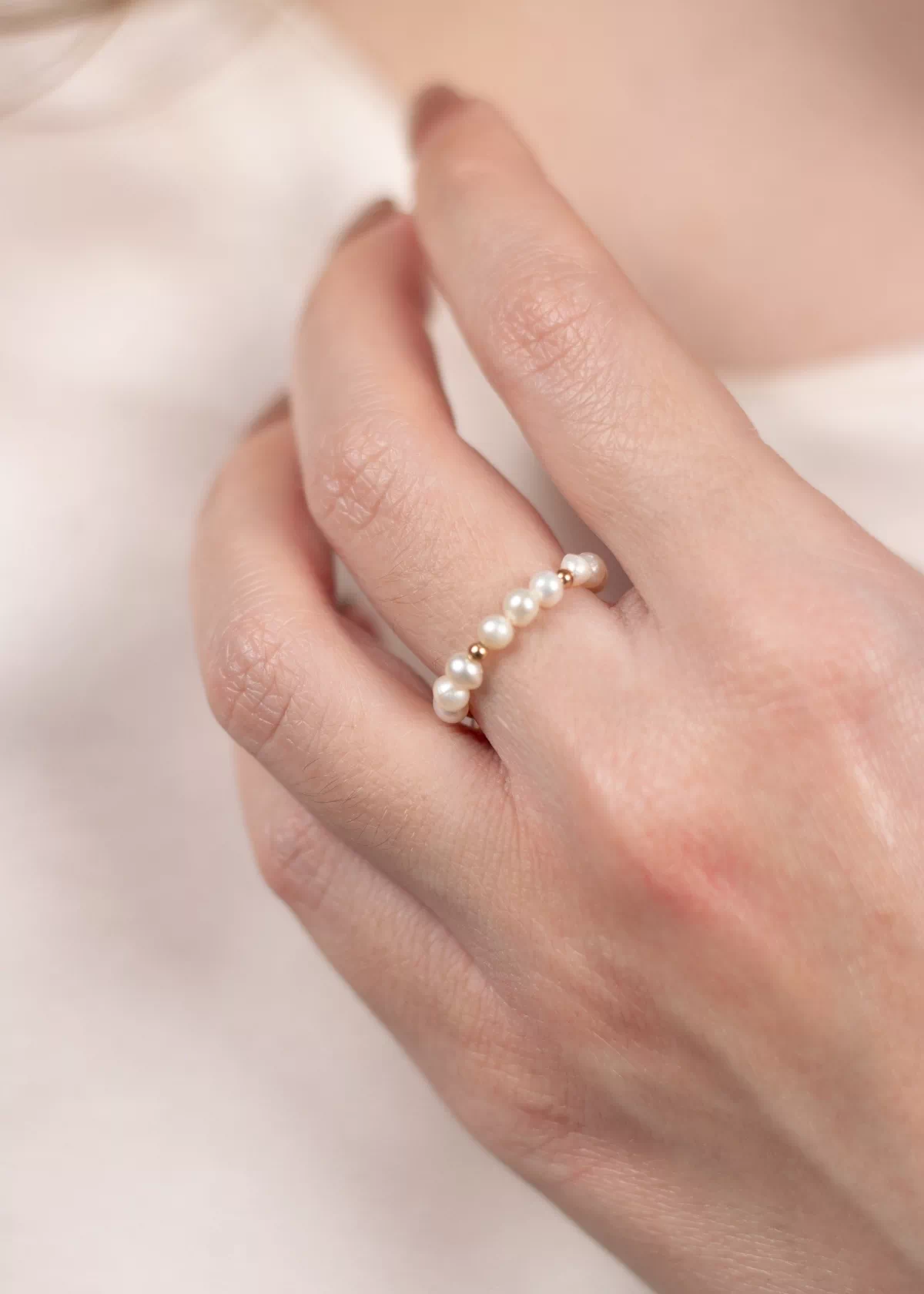 Gros plan de la bague ajustable Sirena en perles de culture blanches et détails dorés, portée sur un doigt.