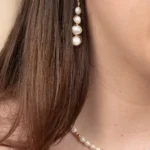 Gros plan sur les boucles d'oreilles Luna en perles blanches et or laminé, portées avec un collier de perles assorti.