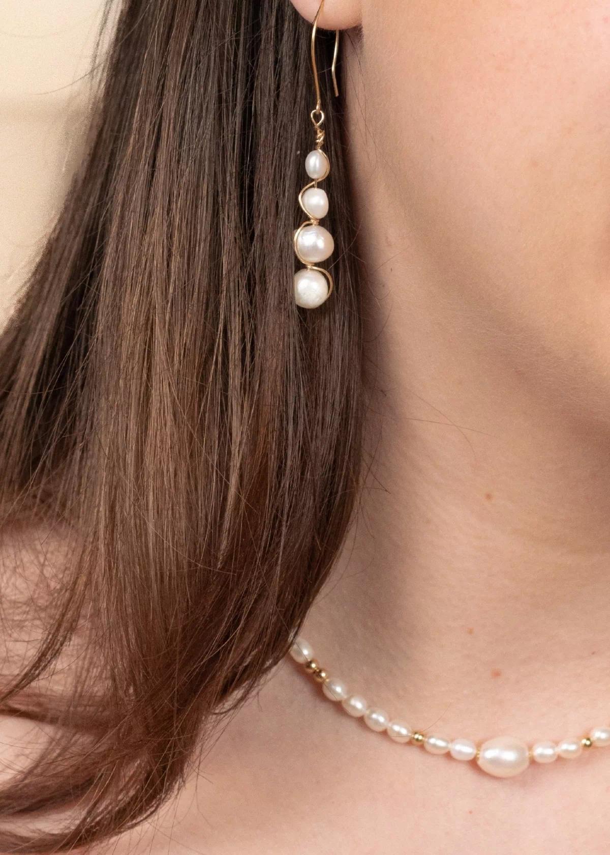 Gros plan sur les boucles d'oreilles Luna en perles blanches et or laminé, portées avec un collier de perles assorti.
