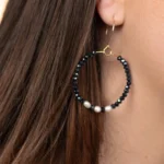 Modèle portant les créoles Éclat en perles bleu marine et blanches, associées à un collier et un bracelet assortis.