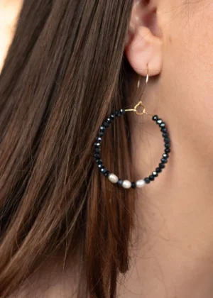 Modèle portant les créoles Éclat en perles bleu marine et blanches, associées à un collier et un bracelet assortis.