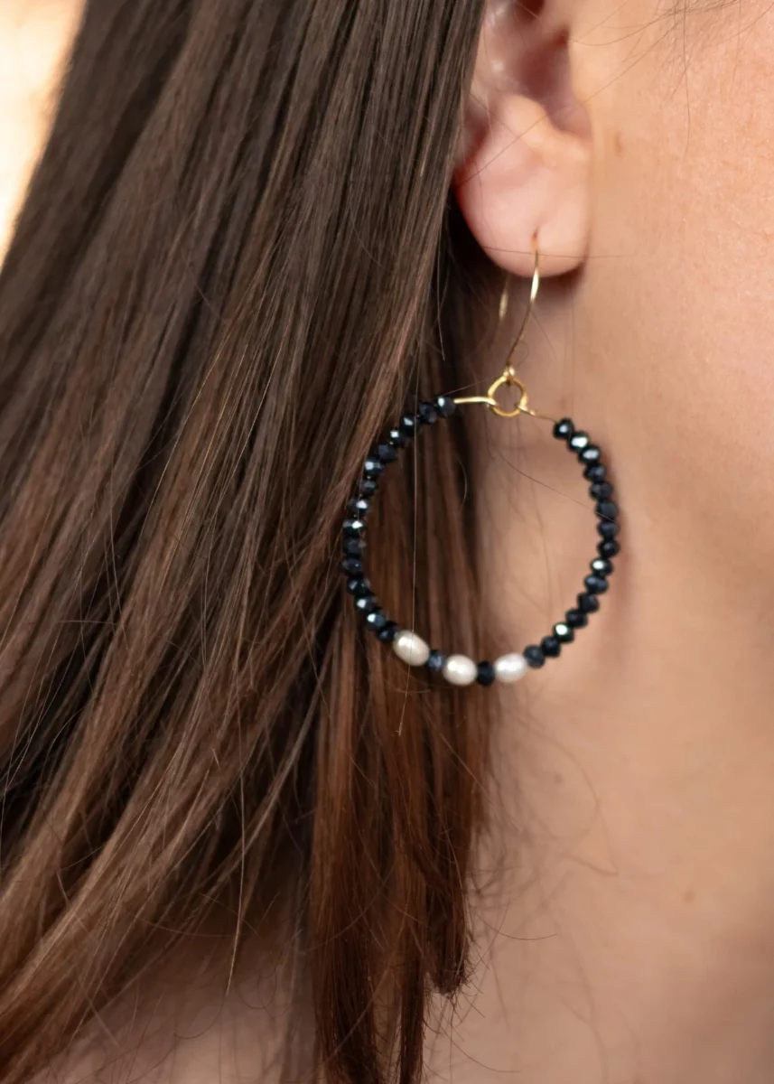 Modèle portant les créoles Éclat en perles bleu marine et blanches, associées à un collier et un bracelet assortis.