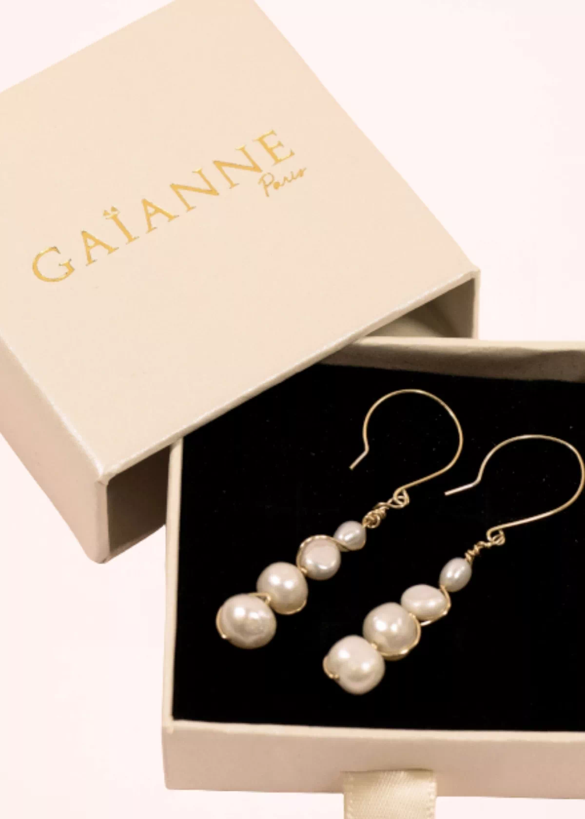 Paire de boucles d'oreilles pendantes Luna en perles de culture blanches et or laminé, présentée dans une boîte cadeau GAÏANNE beige à intérieur noir.