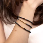 Bracelet collier Nocturne porté en bracelet trois tours au poignet, avec des perles bleu marine et des détails dorés en or laminé.