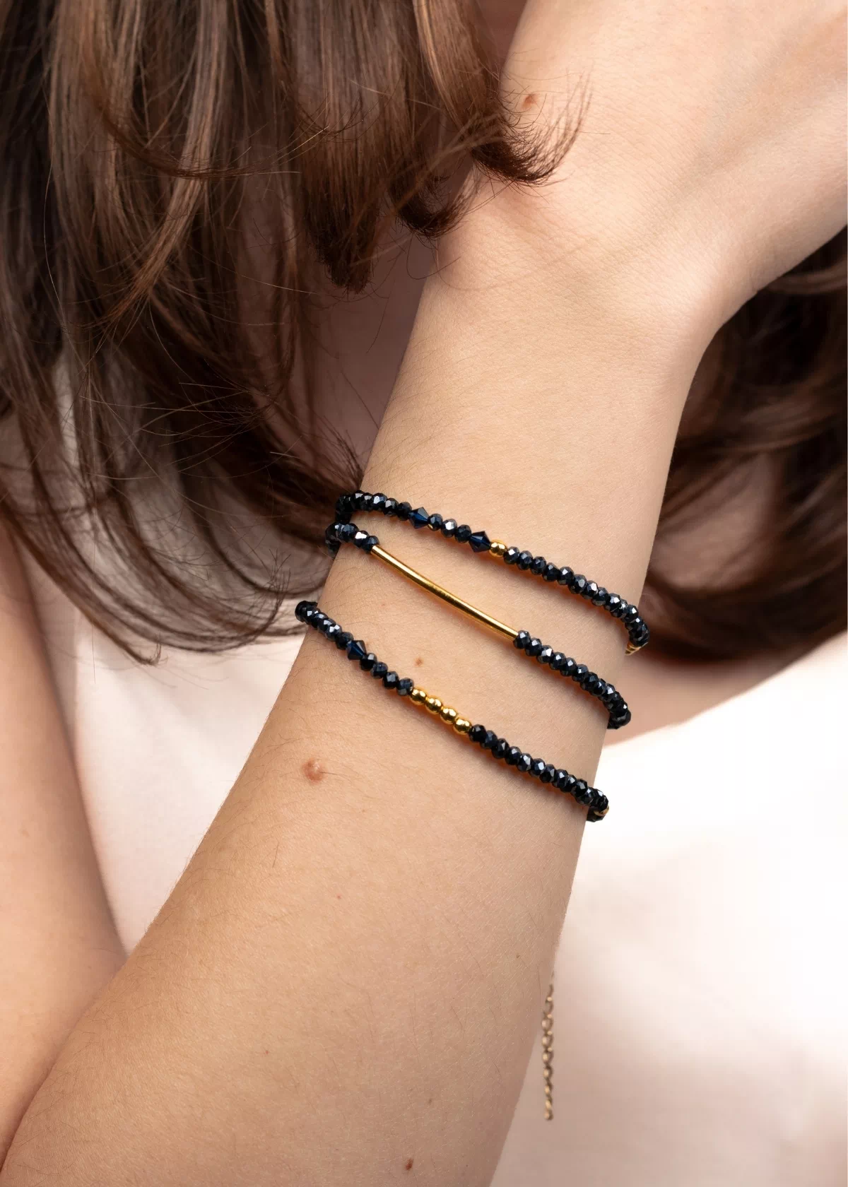 Bracelet collier Nocturne porté en bracelet trois tours au poignet, avec des perles bleu marine et des détails dorés en or laminé.