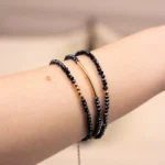 Gros plan du bracelet Nocturne enroulé trois fois autour du poignet, avec des perles facettées bleu marine, des détails dorés et une chaîne d'extension