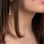 Collier Céleste en perles de culture blanches et chaîne en or laminé, porté autour du cou avec les boucles d'oreilles Luna assorties.