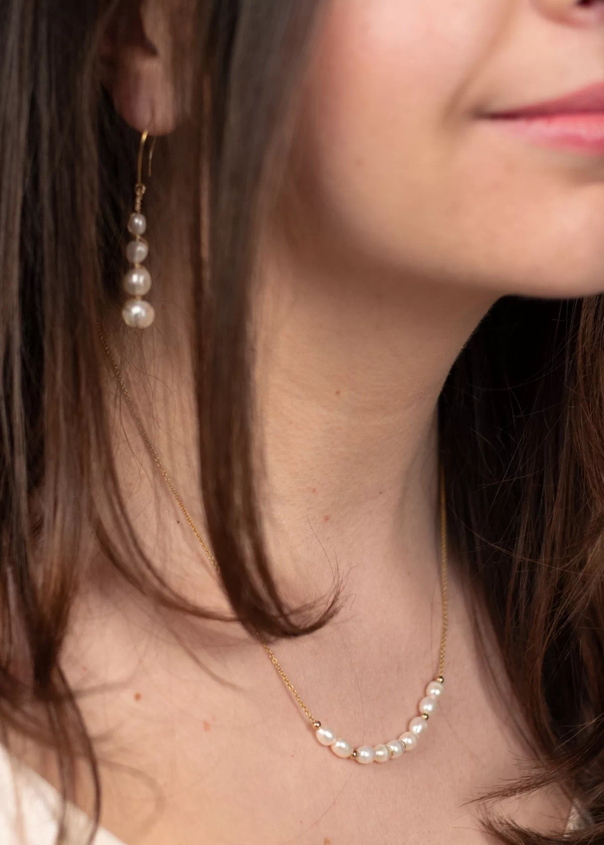 Collier Céleste en perles de culture blanches et chaîne en or laminé, porté autour du cou avec les boucles d'oreilles Luna assorties.