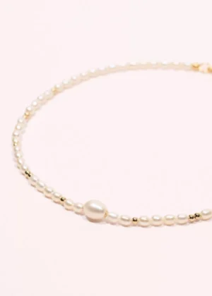 Gros plan du collier Éclipse en perles de culture d'eau douce blanches et or laminé 14 carats, avec une perle centrale plus imposante.