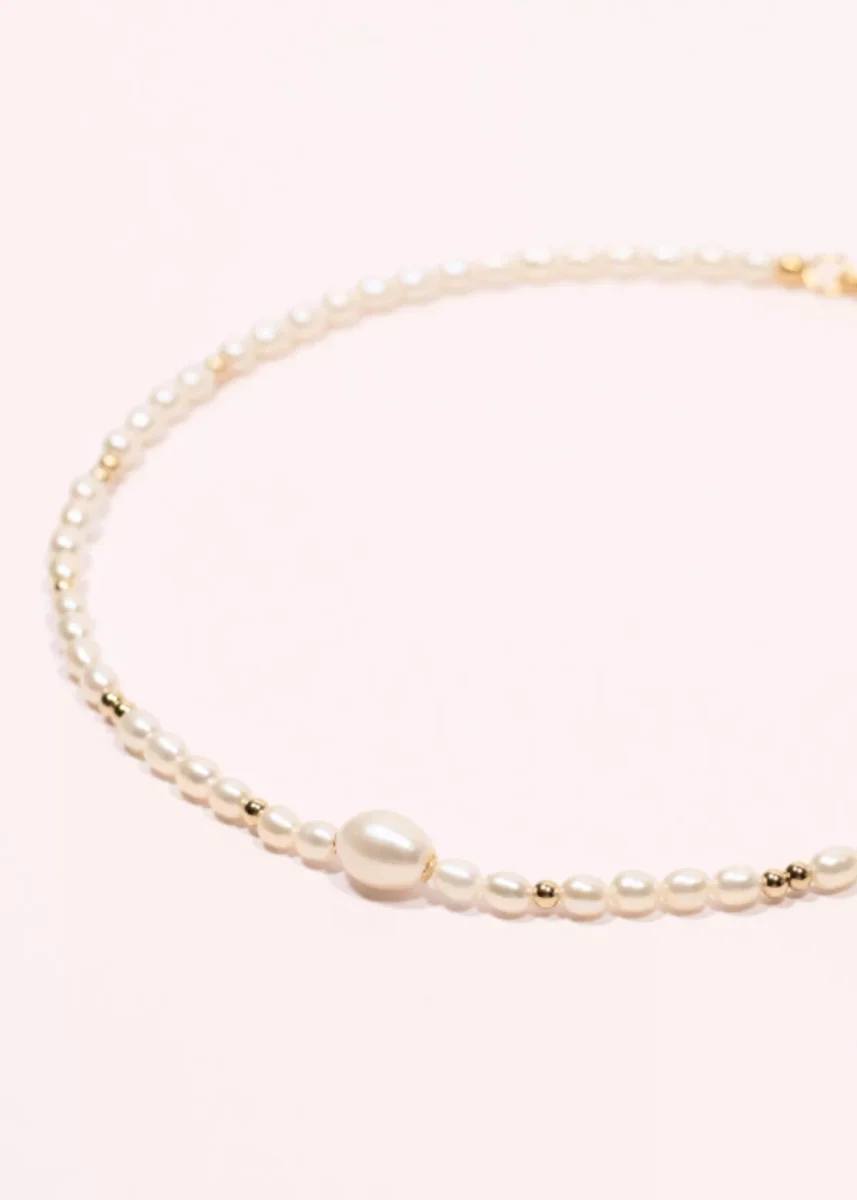 Gros plan du collier Éclipse en perles de culture d'eau douce blanches et or laminé 14 carats, avec une perle centrale plus imposante.