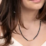 Bracelet collier Nocturne porté autour du cou en collier de perles bleu marine, avec des détails dorés en or laminé 14 carats.