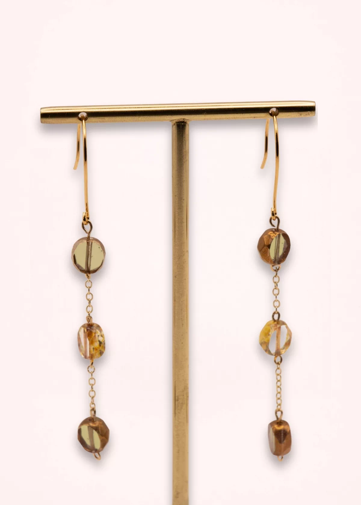 Boucles d'oreilles Nathéa de 8 cm suspendues à un présentoir doré, avec perles de Bohême aux reflets ambrés et chaînes fines en or laminé 14 carats.