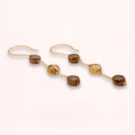 Boucles d'oreilles pendantes Nathéa en perles de verre de Bohême aux nuances miel, caramel et brun, avec chaînes fines dorées et attaches crochets, sur fond clair.