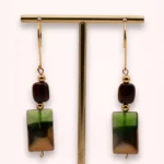 Boucles d'oreilles pendantes Sandria avec pierres naturelles d'œil de tigre brun, perles géométriques vertes en verre de Bohême et crochets dorés en or laminé 14K, sur présentoir.
