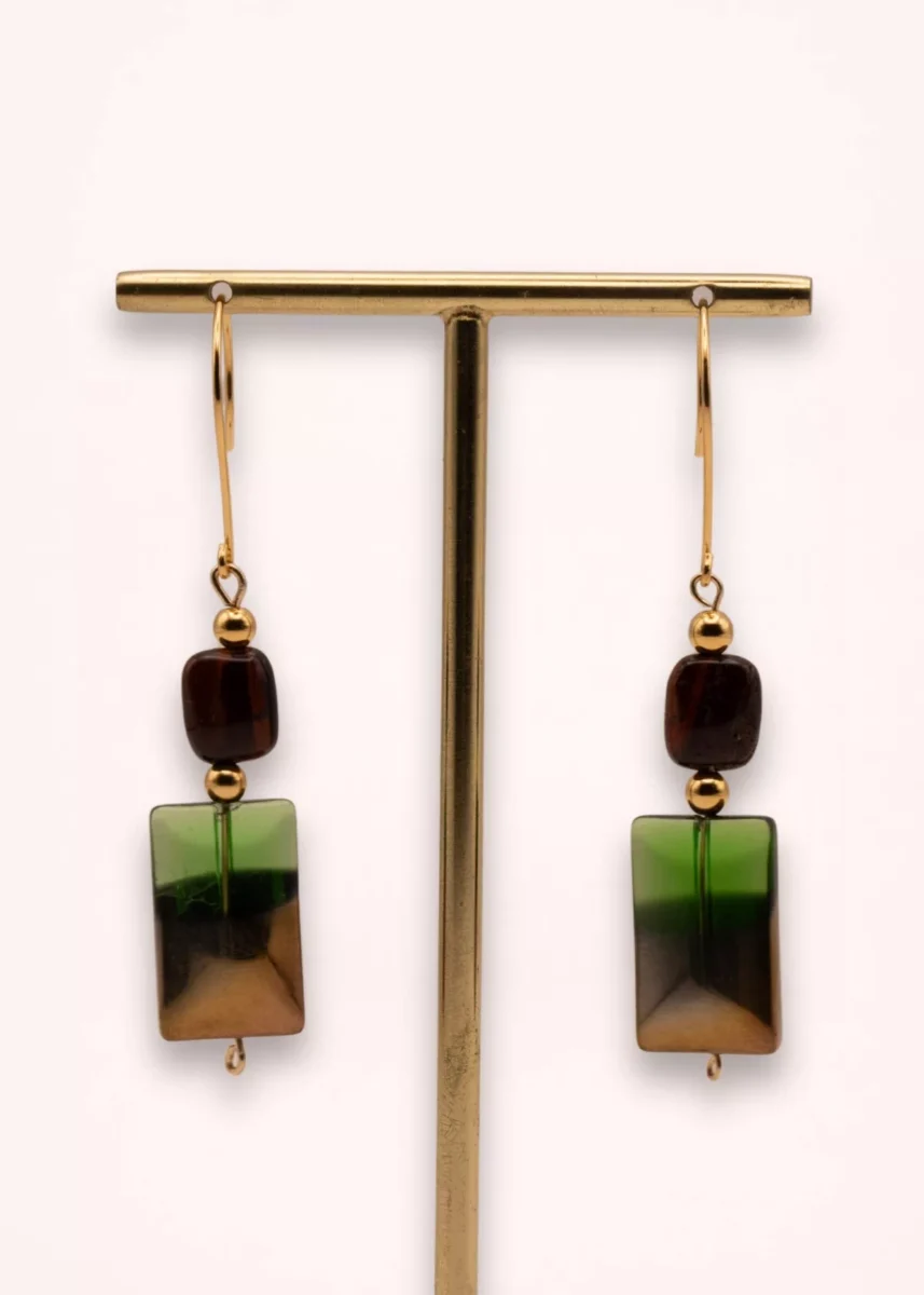 Boucles d'oreilles pendantes Sandria avec pierres naturelles d'œil de tigre brun, perles géométriques vertes en verre de Bohême et crochets dorés en or laminé 14K, sur présentoir.
