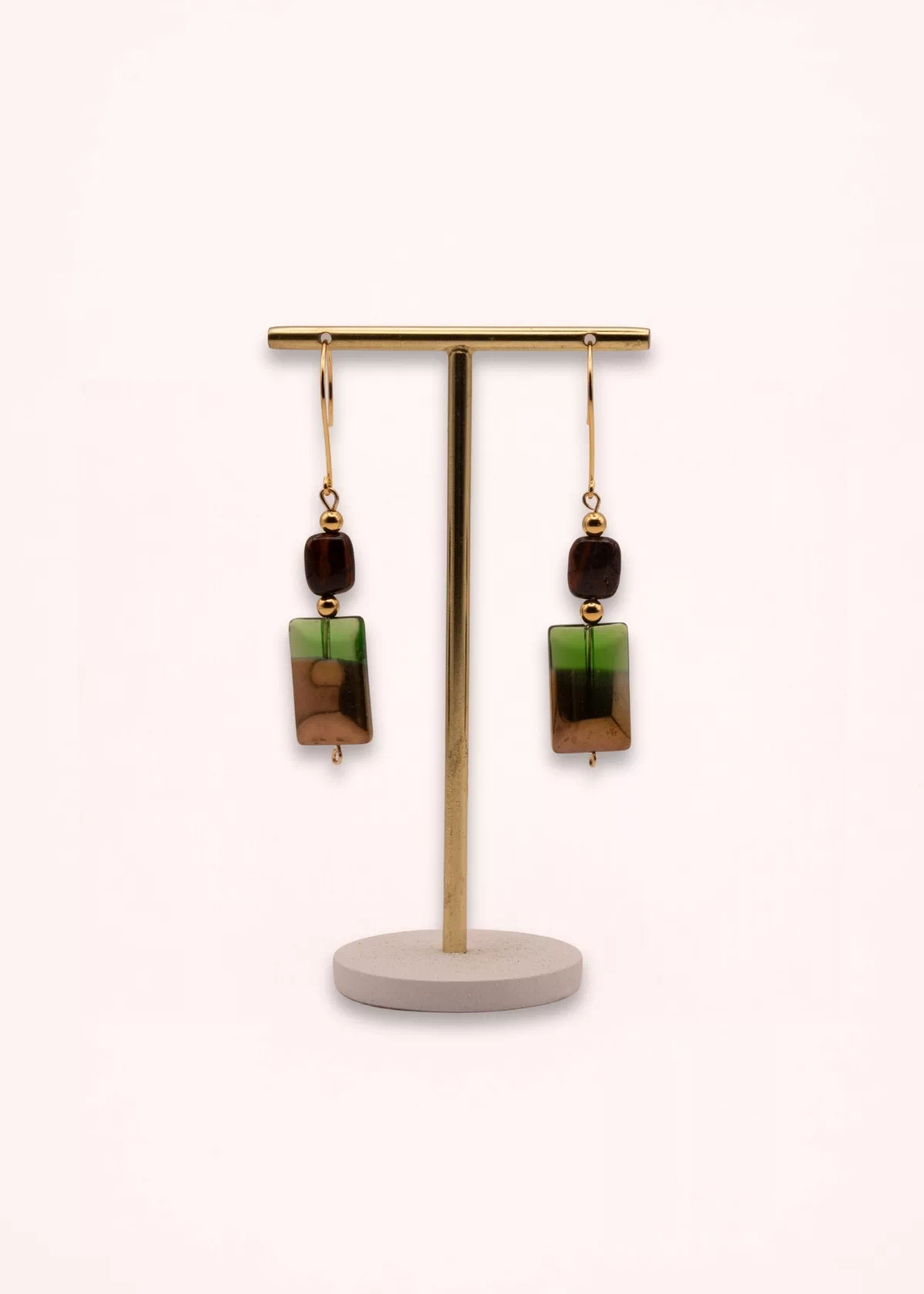 Vue d'ensemble des boucles d'oreilles Sandria de 6,5 cm, suspendues à un présentoir doré sur socle clair, avec perles vertes et brunes et attaches en or laminé.