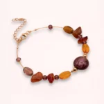 Bracelet Delphéa en pierres naturelles de cornaline et d'agate rouge-orange, avec perle violette en verre de Bohême, détails Swarovski et or laminé 14K, sur fond clair.