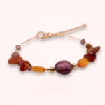 Vue rapprochée du bracelet Delphéa avec sa grande perle violette en verre de Bohême, ses pierres de cornaline et d'agate rouge-orange et ses détails dorés.