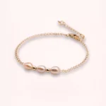 Bracelet Esmée en perles d'eau douce blanches aux reflets nacrés, avec chaîne fine et détails dorés en or laminé 14 carats, sur fond clair.