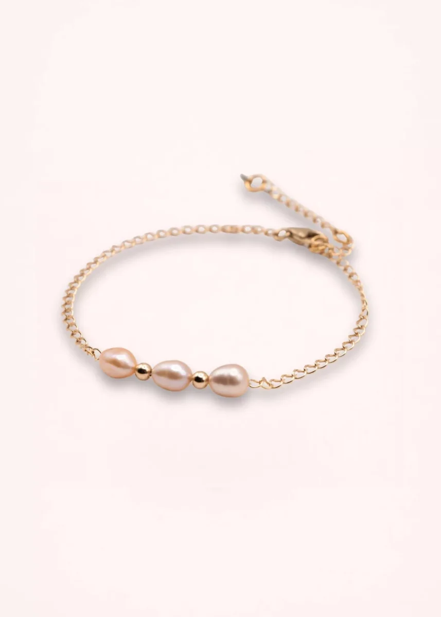 Bracelet Esmée en perles d'eau douce blanches aux reflets nacrés, avec chaîne fine et détails dorés en or laminé 14 carats, sur fond clair.