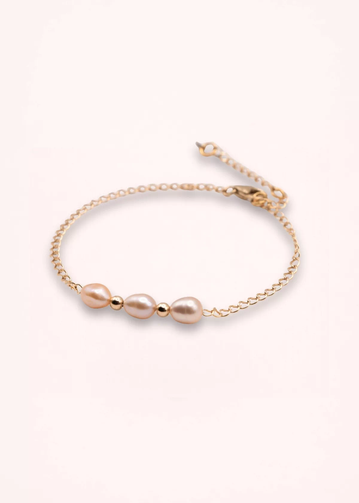 Bracelet Esmée en perles d'eau douce blanches aux reflets nacrés, avec chaîne fine et détails dorés en or laminé 14 carats, sur fond clair.
