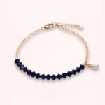 Bracelet Isabélia présenté sur fond clair, avec perles Swarovski bleu profond, perle d'eau douce blanche pendante et chaîne fine ajustable en or laminé.
