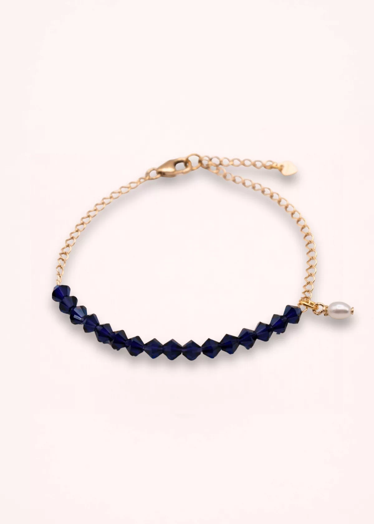 Bracelet Isabélia présenté sur fond clair, avec perles Swarovski bleu profond, perle d'eau douce blanche pendante et chaîne fine ajustable en or laminé.