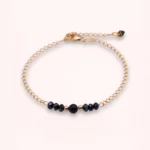 Bracelet Nalia en or laminé 14 carats avec perles bleu nuit en verre de Bohême, détail central en goldstone bleu et chaîne fine ajustable, sur fond clair.