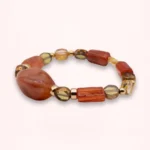 Bracelet Sienna élastique en cornaline naturelle, perles de verre de Bohême aux tons orangés et détails dorés en or laminé 14K, sur fond clair.