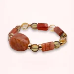 Vue rapprochée du bracelet Sienna montrant sa grande perle centrale en verre de Bohême, ses pierres de cornaline orange et ses perles dorées en or laminé.