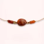 Vue rapprochée du collier Sienna montrant sa grande perle centrale en verre de Bohême, ses perles de cornaline orange et sa chaîne fine en or laminé.