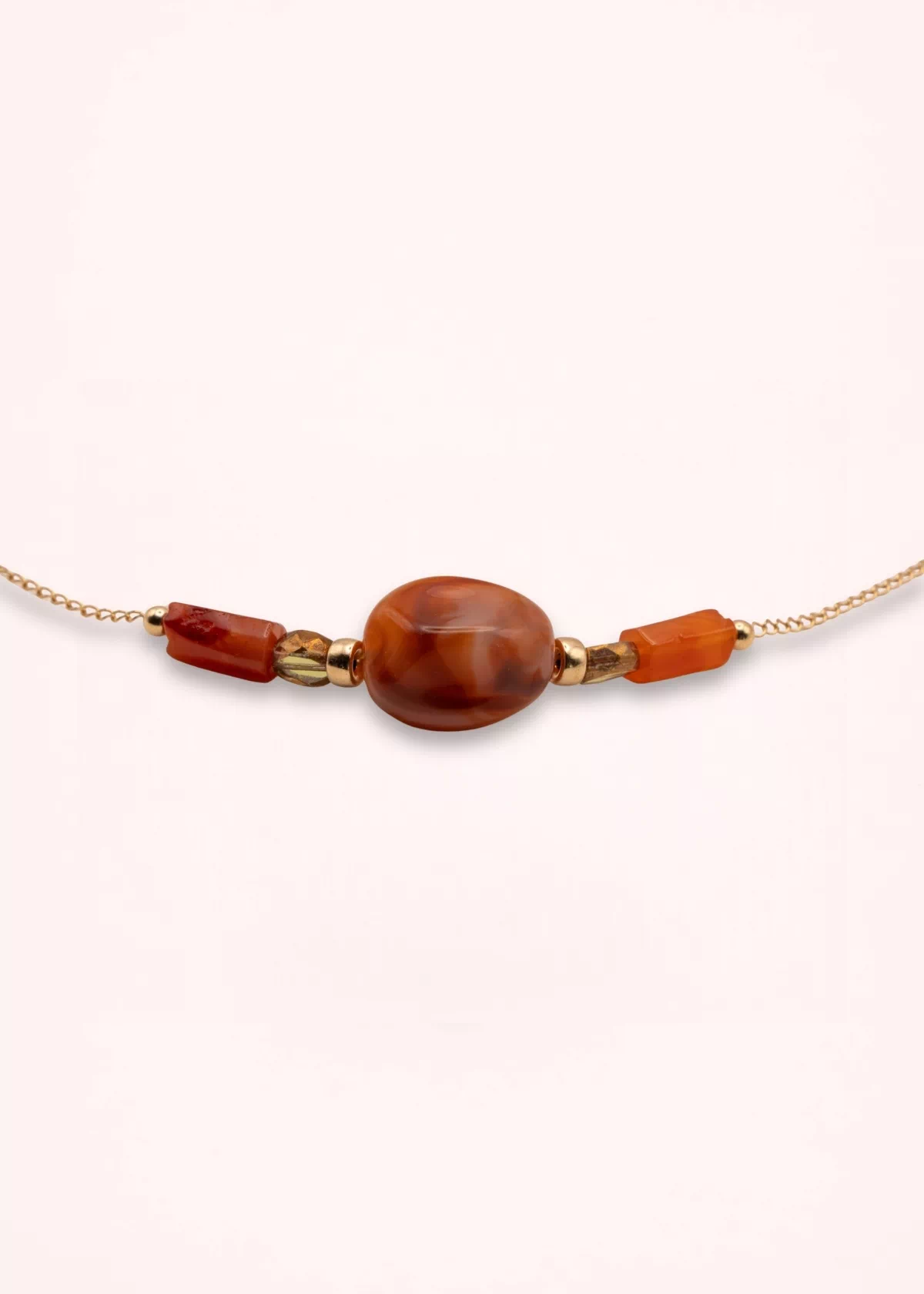 Vue rapprochée du collier Sienna montrant sa grande perle centrale en verre de Bohême, ses perles de cornaline orange et sa chaîne fine en or laminé.
