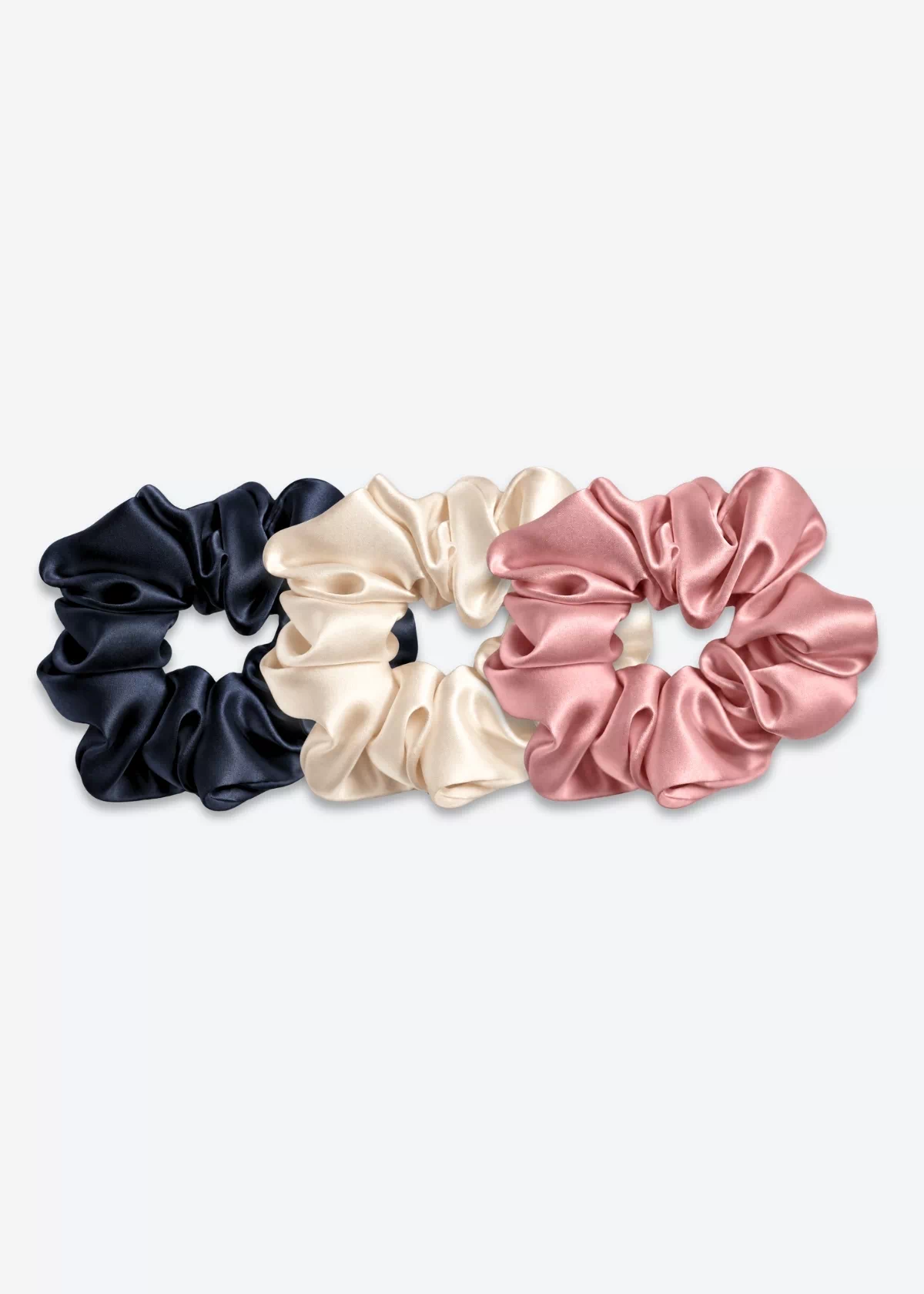 Trois grands chouchous en soie : un bleu nuit, un champagne et un bois de rose.