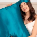 Femme tenant contre elle un grand oreiller en soie Bleu Canard, avec un masque de nuit assorti sur le front.