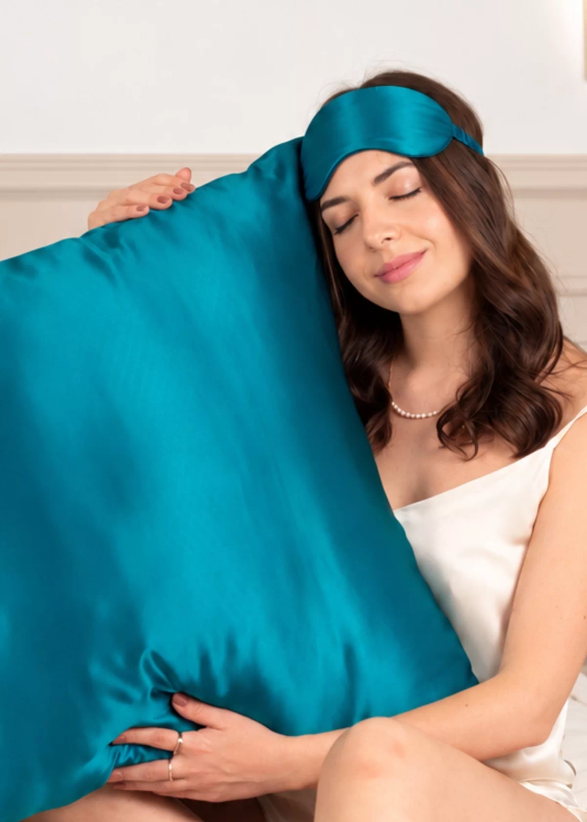 Femme tenant contre elle un grand oreiller en soie Bleu Canard, avec un masque de nuit assorti sur le front.