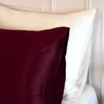Gros plan sur une taie d'oreiller en soie de mûrier Bordeaux posée devant des oreillers blancs.
