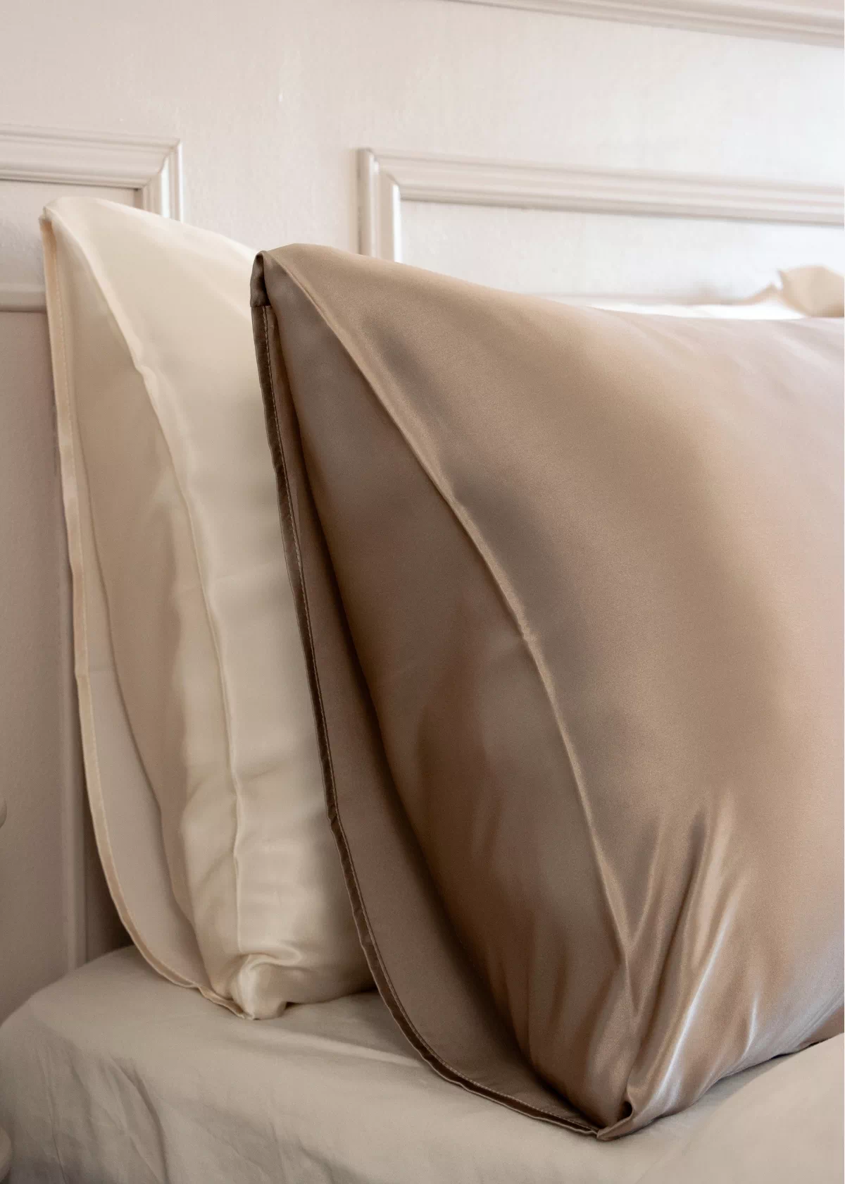 Gros plan sur une taie d'oreiller en soie Taupe au fini lisse et brillant, posée devant des oreillers blancs.