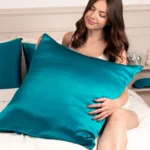 Femme assise sur un lit, caressant un oreiller recouvert d'une taie en soie Bleu Canard.