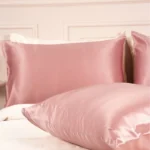 Deux taies d'oreiller en soie de mûrier Bois de Rose disposées sur un lit blanc, aux reflets délicats.