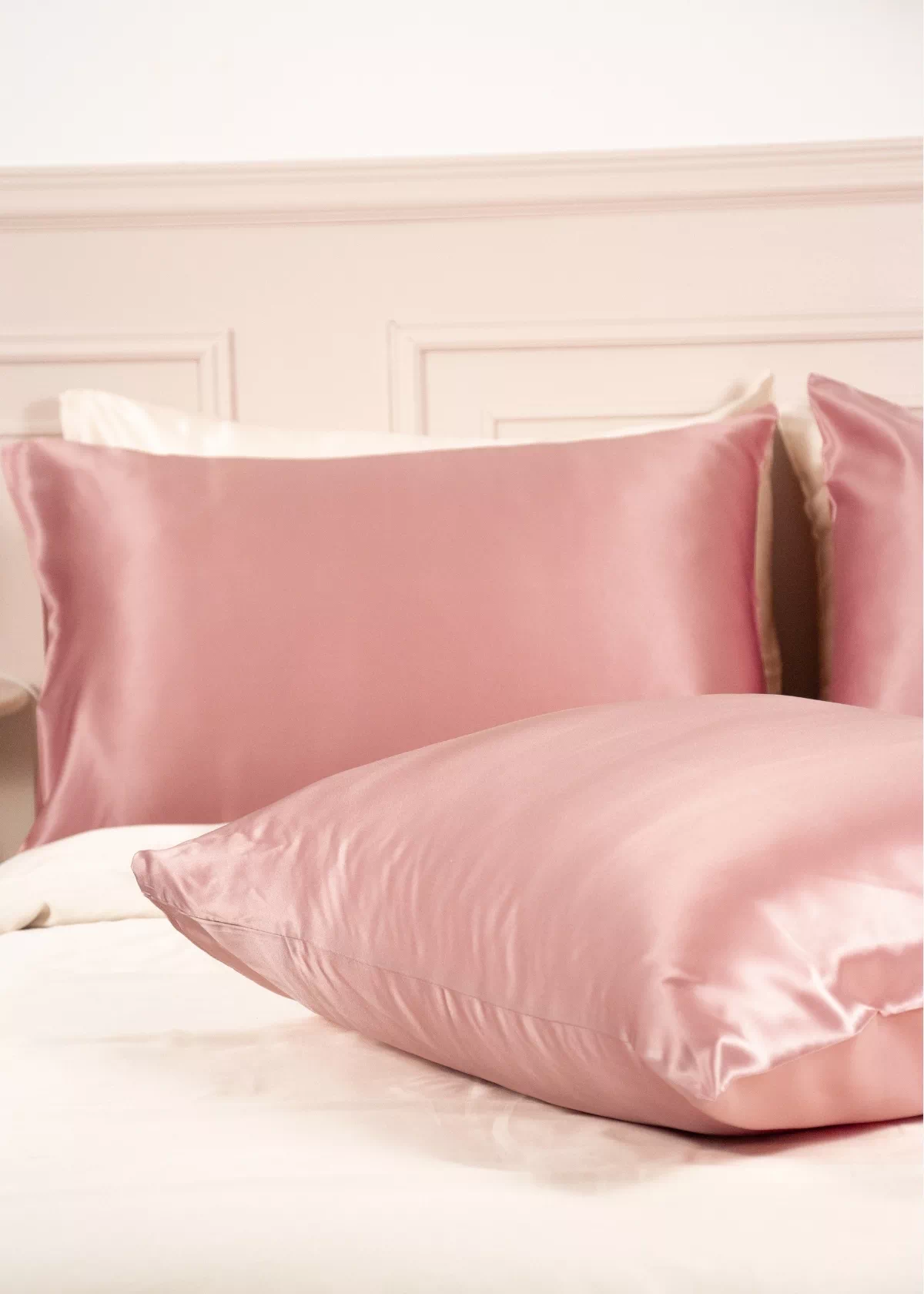 Deux taies d'oreiller en soie de mûrier Bois de Rose disposées sur un lit blanc, aux reflets délicats.